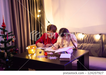 Grandmother and granddaughter enjoy a cozy Christmas evening, writing together by the festive lights. 124207927
