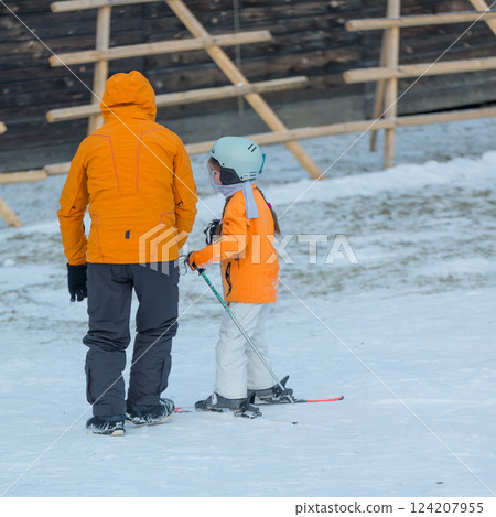 Exciting snowy day filled with learning and joy as a parent teaches a child how to ski at a beautiful winter resort under clear skies 124207955