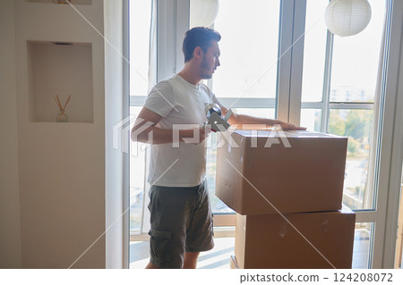 Man standing in living room on day of move to rented home, unbox carton box with belongings. Relocate to new own apartment collect personal things 124208072