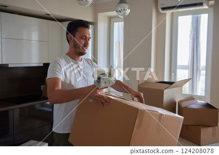 Man standing in living room on day of move to rented home, unbox carton box with belongings. Relocate to new own apartment collect personal things Man standing in living room on day of move to rented home, unbox carton box with belongings. Relocate to new own apartment collect personal things 124208078