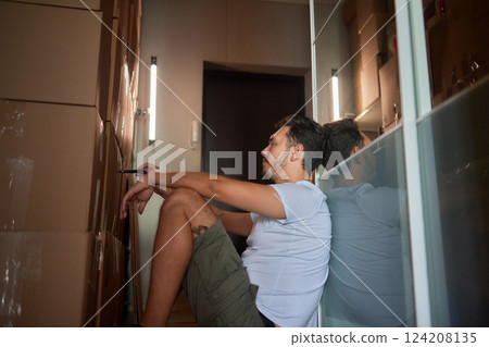 Man standing in living room on day of move to rented home, unbox carton box with belongings. Relocate to new own apartment collect personal things Man standing in living room on day of move to rented home, unbox carton box with belongings. Relocate to new own apartment collect personal things 124208135