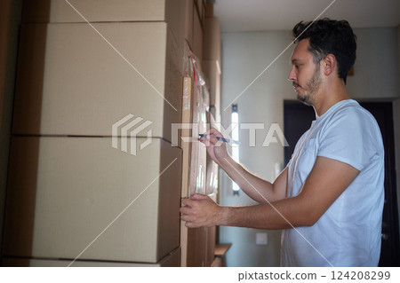 Man standing in living room on day of move to rented home, unbox carton box with belongings. Relocate to new own apartment collect personal things 124208299