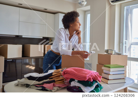 people, moving new place and repair concept - happy african american young woman with many cardboard boxes sitting on floor at home 124208306