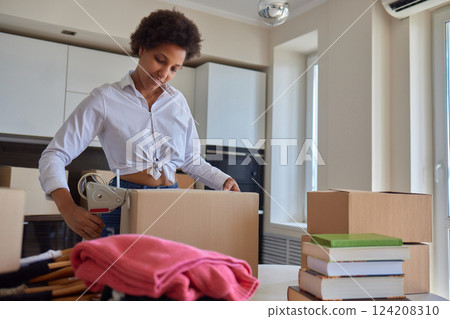 people, moving new place and repair concept - happy african american young woman with many cardboard boxes sitting on floor at home 124208310