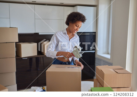 people, moving new place and repair concept - happy african american young woman with many cardboard boxes sitting on floor at home 124208312