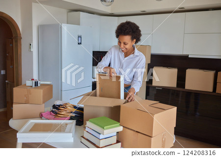 people, moving new place and repair concept - happy african american young woman with many cardboard boxes sitting on floor at home 124208316
