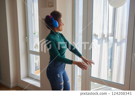 Overjoyed millennial girl wearing headphones have fun moving listening to music relax in living room, happy young woman in earphones dance enjoy leisure weekend at home, stress free concept 124208341
