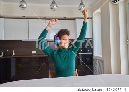 Overjoyed millennial girl wearing headphones have fun moving listening to music relax in living room, happy young woman in earphones dance enjoy leisure weekend at home, stress free concept 124208344
