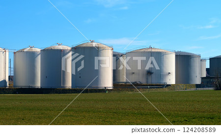 Large storage tanks at an industrial site surrounded by green fields under a clear blue sky during midday Large storage tanks at an industrial site surrounded by green fields under a clear blue sky during midday 124208589