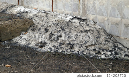 An old snowdrift slowly melting under the warmth of spring reveals a mixture of dirt and debris, resting against an aged wall, marking the transition from winter to warmer days. 124208720