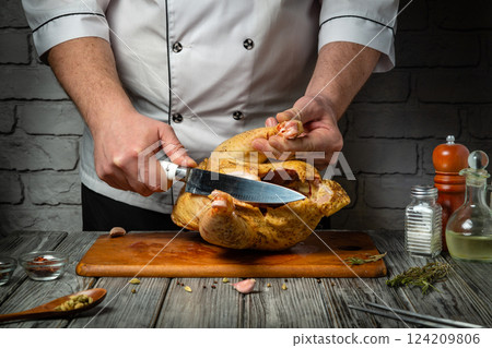 A culinary expert demonstrates their craft, skillfully carving a seasoned chicken on a wooden board. Aromatic herbs and spices surround the preparation area, enhancing the atmosphere 124209806