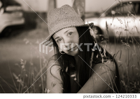 A beautiful cute young woman in a straw hat resting on the lawn among grasses in summer. Sepia female portrait. Summertime vacation trip, journey. 124210333
