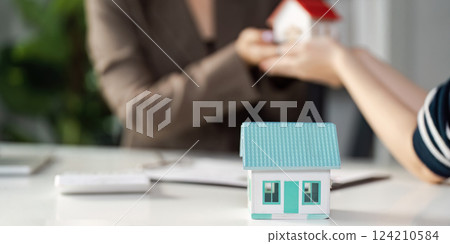 Real estate agent handing over a model house to a client, discussing property options and investment potential. Real estate agent handing over a model house to a client, discussing property options and investment potential. 124210584