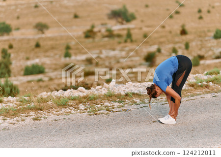 Determined Female Athlete Stretching After an Intense Run Through Rugged Mountain Terrain. 124212011