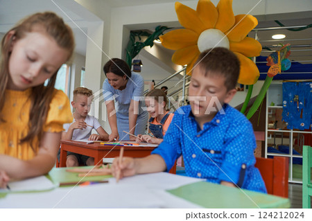 Creative kids during an art class in a daycare center or elementary school classroom drawing with female teacher. 124212024