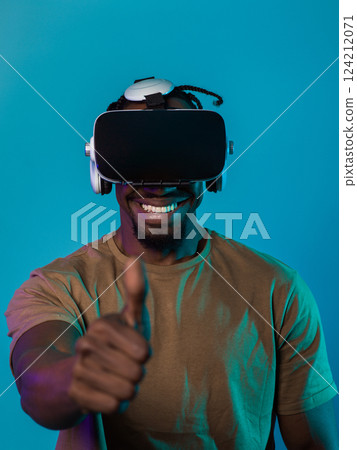African American man wearing virtual reality glasses expresses satisfaction and impressed delight, gesturing with his hand pointed upward, while standing isolated against a vibrant yellow background 124212071