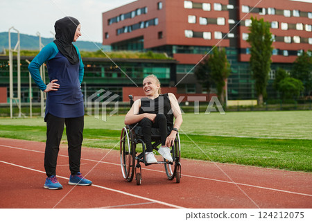 A Muslim woman wearing a burqa resting with a woman with disability after a hard training session on the marathon course 124212075