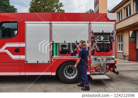 A dedicated firefighter preparing a modern firetruck for deployment to hazardous fire-stricken areas, demonstrating readiness and commitment to emergency response 124212096