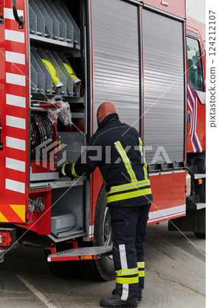 A firefighter meticulously prepares a modern firetruck for a mission to evacuate and respond to dangerous situations, showcasing the utmost dedication to safety and readiness in the face of a fire 124212107