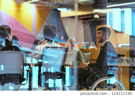 In a modern glass startup office, a wheelchair-bound director leads a successful meeting with colleagues, embodying inclusivity and teamwork. In a modern glass startup office, a wheelchair-bound director leads a successful meeting with colleagues, embodying inclusivity and teamwork. 124212198