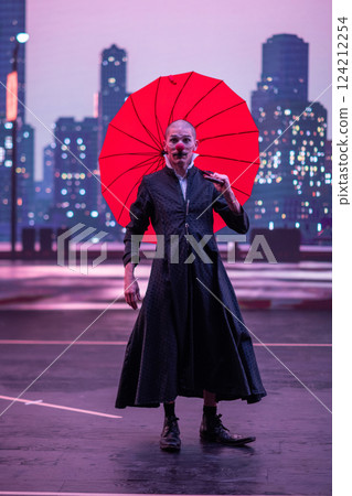 Mysterious Clown Performer with Red Umbrella in Urban Nightscape. Mysterious Clown Performer with Red Umbrella in Urban Nightscape. 124212254