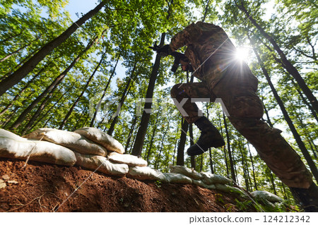 An elite soldier adeptly clears military barriers in the perilous wooded terrain, showcasing tactical skill and agility during specialized training An elite soldier adeptly clears military barriers in the perilous wooded terrain, showcasing tactical skill and agility during specialized training 124212342