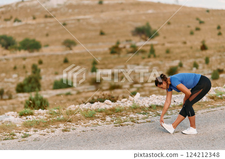 Determined Female Athlete Stretching After an Intense Run Through Rugged Mountain Terrain. Determined Female Athlete Stretching After an Intense Run Through Rugged Mountain Terrain. 124212348