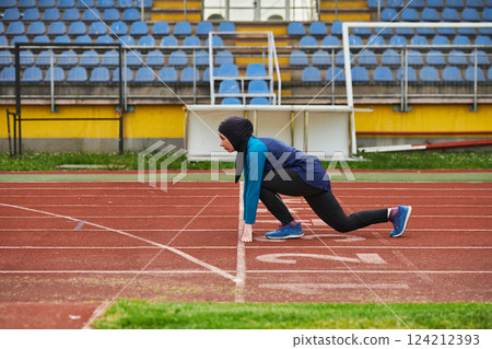 Muslim woman in burqa in sporty Muslim clothes in starting pose for running 124212393