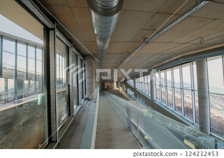 A captivating view of a modern business building under construction, showcasing its raw industrial interior with exposed steel beams and concrete walls bathed in the warm, golden hues of a sunset 124212453