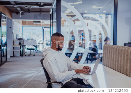 In a modern office setting, an African American businessman is diligently working on his laptop, embodying determination, ambition, and productivity in his professional environmen 124212493