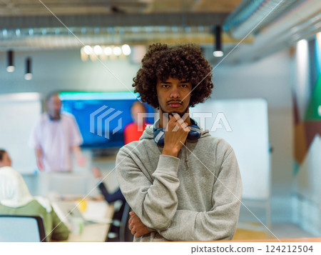 In a modern office environment, an African American young entrepreneur with headphones engages in work, while in the background, his dedicated colleagues exemplify teamwork and collaboration In a modern office environment, an African American young entrepreneur with headphones engages in work, while in the background, his dedicated colleagues exemplify teamwork and collaboration 124212504