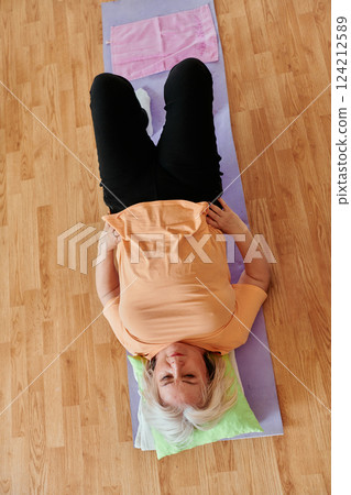 Senior woman practicing stretching and meditation on the floor, focusing on proper alignment and relaxation. 124212589
