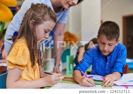 Creative kids during an art class in a daycare center or elementary school classroom drawing with female teacher. 124212711