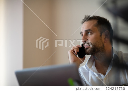 A businessman talking on his smartphone while seated in an office, showcasing his professional demeanor and active communication. 124212730