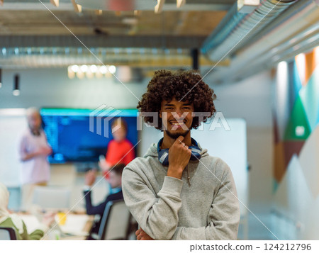 In a modern office environment, an African American young entrepreneur with headphones engages in work, while in the background, his dedicated colleagues exemplify teamwork and collaboration 124212796