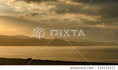 Sunset over the tranquil lake reflecting distant mountains in a golden glow 124212813