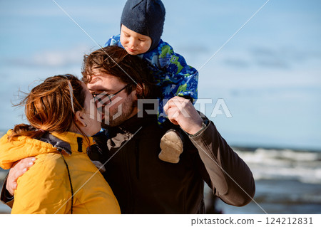 A happy family strolls along a chilly autumn beach, with their young son joyfully running ahead, creating lasting memories as the crisp wind and soothing waves embrace them in a moment of pure 124212831