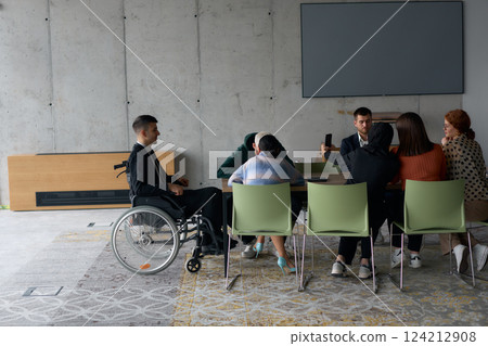 A diverse group of business professionals, including a man in a wheelchair, collaborate during a meeting in a modern office environment. A diverse group of business professionals, including a man in a wheelchair, collaborate during a meeting in a modern office environment. 124212908
