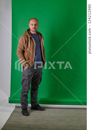 Middle aged bald man in casual attireposes confidently against a green studio backdrop. 124212990