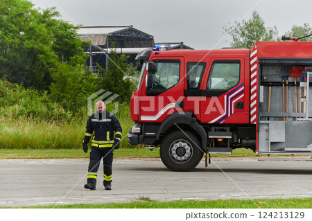 A symbolically brave firefighter strides forward with unwavering courage, epitomizing dedication and leadership, while behind him, a modern firetruck stands ready for firefighting actions, capturing 124213129