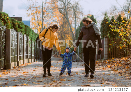 A loving couple strolls through a sunlit park with their young son, surrounded by the vibrant colors of autumn, enjoying a joyful and peaceful family moment together. A loving couple strolls through a sunlit park with their young son, surrounded by the vibrant colors of autumn, enjoying a joyful and peaceful family moment together. 124213157