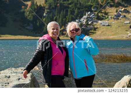 Senior women hikers standing on mountain enjoying a trekking day - Smiling climbing tourists enjoying holidays and healthy lifestyle - Freedom, success sport concept 124213235