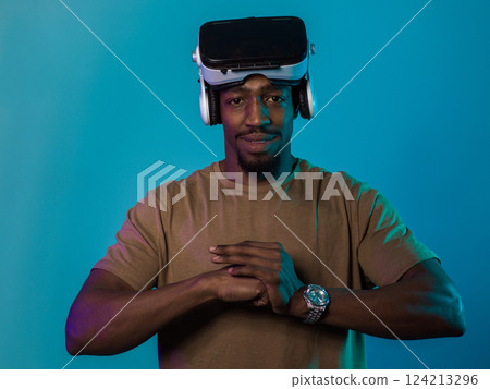 In an avant-garde scene, an African American man engages in cutting-edge virtual reality gaming, utilizing VR glasses to immerse himself in futuristic boxing games, set against a vivid blue background In an avant-garde scene, an African American man engages in cutting-edge virtual reality gaming, utilizing VR glasses to immerse himself in futuristic boxing games, set against a vivid blue background 124213296