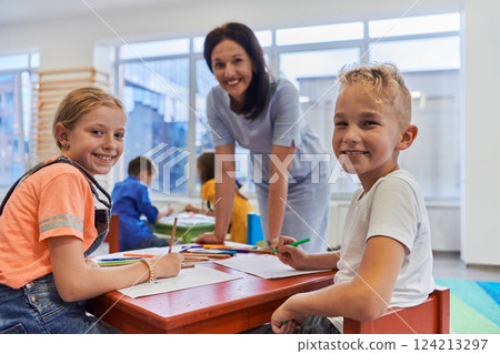 Creative kids during an art class in a daycare center or elementary school classroom drawing with female teacher. Creative kids during an art class in a daycare center or elementary school classroom drawing with female teacher. 124213297