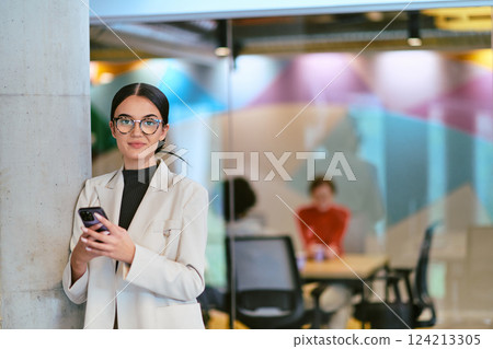 In a modern glass office, a contemporary businesswoman effortlessly multitasks, using her smartphone, while surrounded by colleagues, illustrating the dynamics of corporate life and technology In a modern glass office, a contemporary businesswoman effortlessly multitasks, using her smartphone, while surrounded by colleagues, illustrating the dynamics of corporate life and technology 124213305