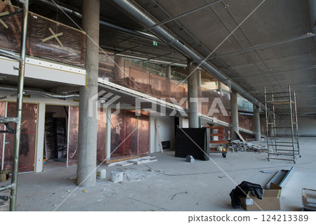 A captivating view of a modern business building under construction, showcasing its raw industrial interior with exposed steel beams and concrete walls bathed in the warm, golden hues of a sunset 124213389