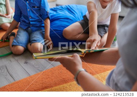 A happy female teacher sitting and playing hand games with a group of little schoolchildren 124213528