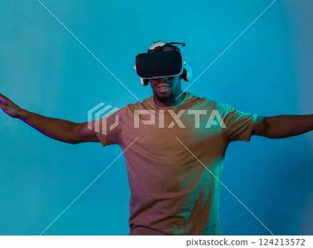 African American man dons VR glasses, engrossed in a virtual reality simulation, gesturing with hands, against a striking blue background, highlighting the fusion of cutting-edge technology and African American man dons VR glasses, engrossed in a virtual reality simulation, gesturing with hands, against a striking blue background, highlighting the fusion of cutting-edge technology and 124213572