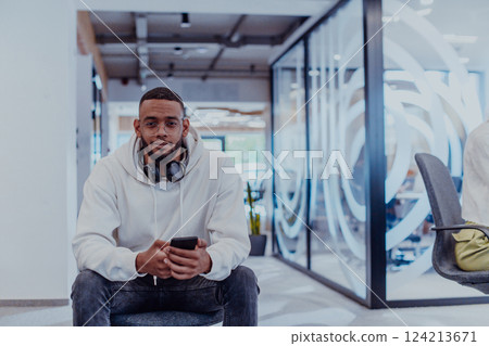 African American businessman wearing headphones while using a smartphone, fully engaged in his work at a modern office, showcasing focus, productivity, and contemporary professionalism 124213671