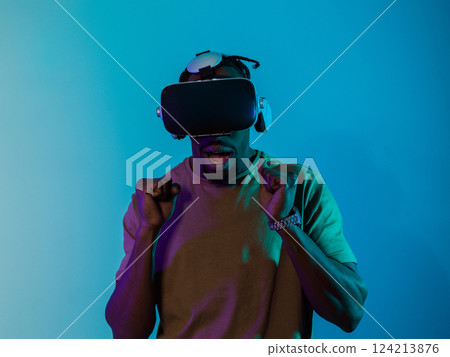 African American man immerses himself in a thrilling horror gaming experience using VR glasses, creating an isolated and intense atmosphere against a striking blue background 124213876